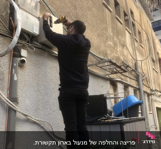 אדם משתמש במקדחה על קיר חיצוני